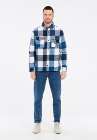 Camicia di flanella a quadri blu e bianca, con due tasche frontali e colletto button-down. Abbinata a jeans blu e scarpe da ginnastica.