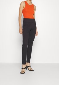 Orange ribbad linne i kombination med svarta slim-fit byxor och svarta klacksandaler. Outfits har en elegant design och minimalistisk stil.