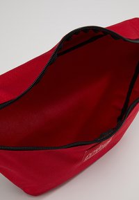 Red fabric bag with a smooth texture, zippered closure, and black trim. Interior is unlined, offering ample storage space.