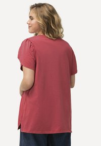 Kortærmet, burgunder bomulds T-shirt med pufærmer, sideskårne slids ved kanten og en afslappet pasform. Bagfra ses en glat tekstur og et afslappet design.
