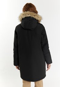 Fekete párnázott parka kabát, szőrme díszítésű kapucnival, hosszú ujjakkal és combközép hosszúsággal. Simább textúra és minimalista dizájn.