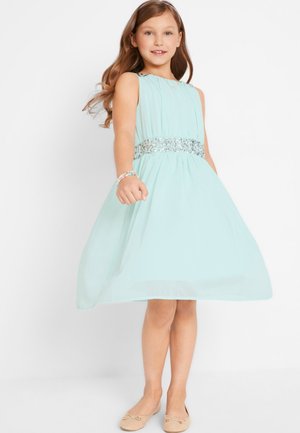 Robe vert menthe avec une jupe évasée, une ceinture en sequins et une coupe sans manches. Associée à des ballerines beiges et un bracelet multicolore.