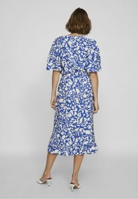 Modré midi šaty s květinovým vzorem, krátkými nafouknutými rukávy, staženým pasem a volánkovým lemem. Tkanina vypadá lehká a texturovaná.