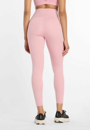 Light pink high-waisted leggings in a smooth, stretchy fabric, paired with black athletic shoes featuring a thick sole and laces.
