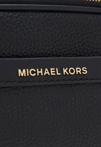 Borsa in pelle nera texturizzata con una placca del logo dorato "MICHAEL KORS". Presenta una chiusura con zip e finiture lisce a contrasto.