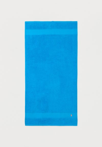 Φωτεινή μπλε ορθογώνια πετσέτα με δύο οριζόντιες λωρίδες κοντά στις άκρες και μικρό πορτοκαλί λογότυπο στην κάτω δεξιά γωνία.