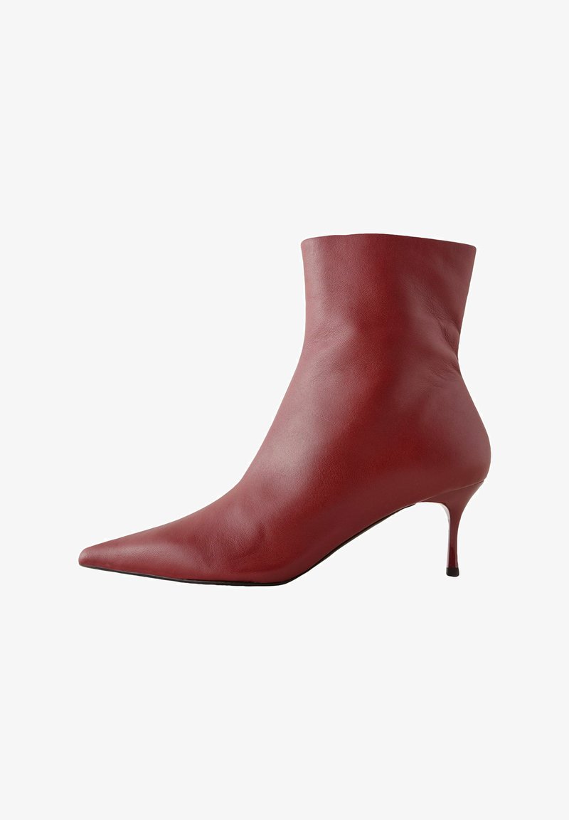 Botte cheville en cuir rouge avec un bout pointu, une tige ajustée et un talon fin. Texture lisse, design élégant et semelle noire à fort contraste.