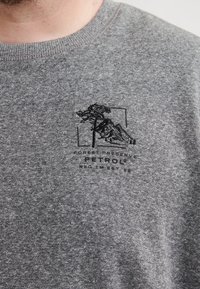 Sudadera gris con una tela texturizada que presenta un diseño bordado en negro de un árbol y una montaña con la palabra "PETROL" debajo.