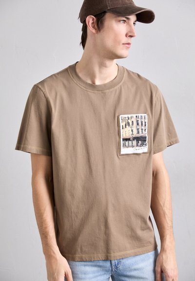 Pruun puuvillane T-särk, millel on ruudukujuline tasku ja linna vaatega trükk. Lühikesed varrukad ja lõdvestunud istuvus. Heledapoolne teksashorts.