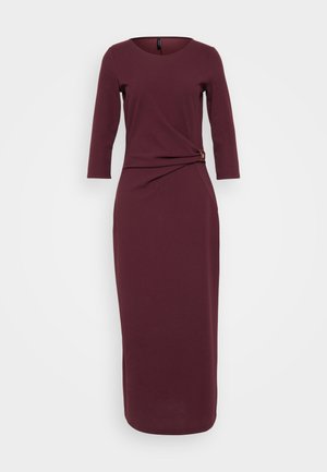 Burgundy långärmad klänning med rund halsringning, åtsittande midja, draperad detalj framtill och en subtil guldaccent på sidan. Slät textur.