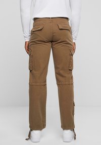 Pantalons cargo marron avec plusieurs poches latérales, une conception ajustée aux chevilles et des détails à cordons, associés à des baskets blanches.