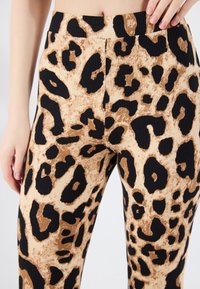 Leggingse s uzorkom leoparda u mekanom, rebrastom materijalu. Imaju upečatljiv crni i smeđi uzorak na svijetlosmeđoj pozadini. Vidljiv visok struk.