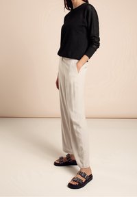 Top negro de manga larga texturizado, pantalones anchos de color beige claro con bolsillos, y sandalias negras con detalles metálicos.