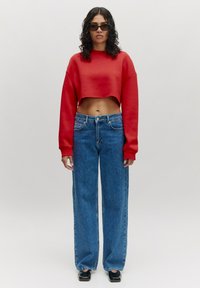 Rode cropped sweatshirt, blauwe wijde jeans en zwarte schoenen. De outfit heeft een eenvoudig ontwerp met een gladde textuur en zonder zichtbare patronen.