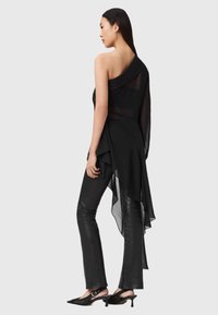 Asymmetrisk svart topp i gjennomsiktig stoff, lagdelt design med flytende draperinger, kombinert med tettsittende svarte skinnbukser og spisse hæler.