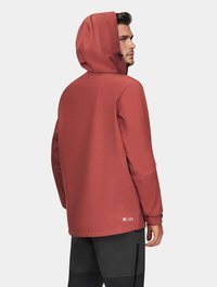 Czerwona wodoodporna kurtka z kapturem, regulowanym sznurkiem i bocznymi kieszeniami. Gładka tekstura i luźny krój, w zestawieniu z czarnymi spodniami.