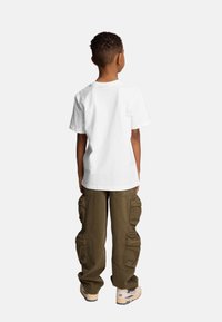 Biała bawełniana koszulka z krótkim rękawem, zestawiona z oliwkowymi spodniami cargo z wieloma kieszeniami. Obuwie jest beżowe z niebieskimi akcentami.