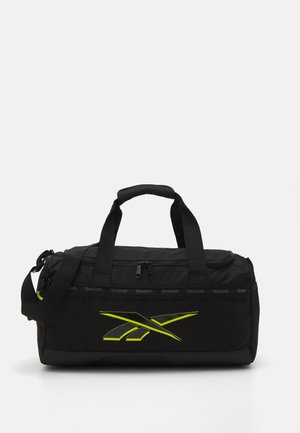 Černá sportovní taška vyrobená z odolné tkaniny, s uzavíratelným vrškem, dvojitými uchy a výrazným žlutým logem Reebok na přední straně.