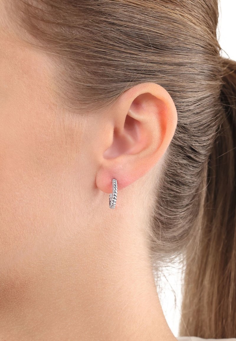 Orecchino a cerchio in argento con un design texturizzato, che presenta un motivo intrecciato. L'orecchino è rotondo e liscio, indossato nel lobo.