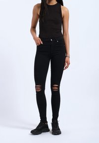 Svarta ripped skinny jeans med hög midja, tillverkade av denim. Matchas med en svart ärmlös topp och svarta träningsskor.