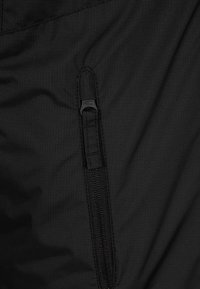 Svart tyg med en texturerad yta som har en ficka med dragkedja. Dragkedjan är dold och smälter in i materialet för en stilren look.