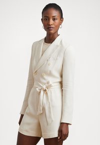 Κρέμα διπλής όψης σακάκι με ζώνη, μακριά μανίκια, πλαϊνές τσέπες και απαλό ύφασμα σε συνδυασμό με ριγέ μπλούζα από κάτω.