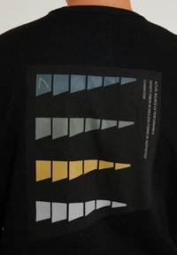 Felpa nera con una grafica stampata sulla schiena. Presenta forme geometriche in teal, grigio, giallo e bianco con del testo lungo il lato destro.