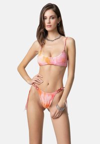 Set di bikini con motivo tie-dye nei toni del rosa e dell'arancione; il top ha spalline sottili e il fondo presenta lacci laterali con dettagli in metallo.