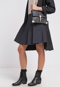 Svart texturerad kjol med en utsvängd design, kombinerad med svarta ankelstövlar. En mörk kofta och en strukturerad svart handväska med gulddetaljer fulländar outfiten.