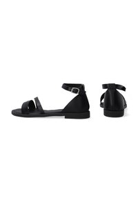 Zwarte platte sandalen met verstelbare enkelriem, met meerdere overlappende banden over de voet en een platte rubbersole.