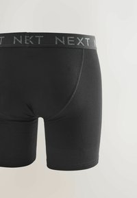 Black boxer briefs with stitched seams and an elastic waistband printed with the brand name "NEXT" in gray.
