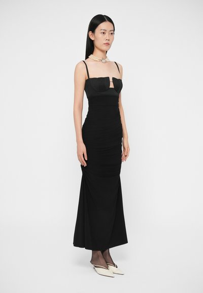 Vestito nero con corpetto aderente e gonna arricciata, caratterizzato da spalline sottili e scollo a cuore. Indossato con una collana di perle e tacchi bianchi.