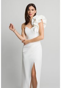 Biała suknia wieczorowa z dopasowanym topem, jednym dużym falbaniastym ramieniem i wysokim rozcięciem na udzie. Gładki materiał z marszczeniami.
