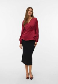 Bourgogne satin indpakningsbluse med lange ærmer og flæse-detalje, kombineret med en tætsiddende sort midi-nederdel og bourgogne spidse stiletter.