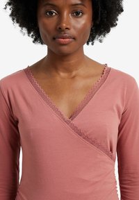 Long-sleeve, V-neck top in dusty rose, made of soft material. Features delicate lace trim along the neckline and wrap design.