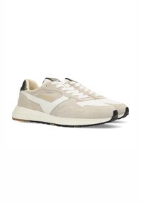 Zapatillas beige de ante y cuero, con una franja lateral blanca, detalles en negro en el talón y una suela blanca con agarre texturizado.