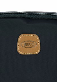 Borsa in tessuto nero con una toppa in pelle con marchio impresso e cuciture beige lungo i bordi. Cerniera nella parte superiore.