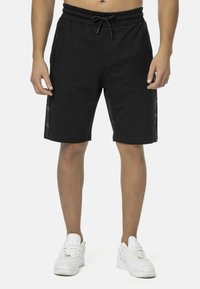Schwarze Shorts aus Baumwolle mit einem elastischen Bund und Kordelzug. Seitliche Streifen mit strukturierten Mustern.
