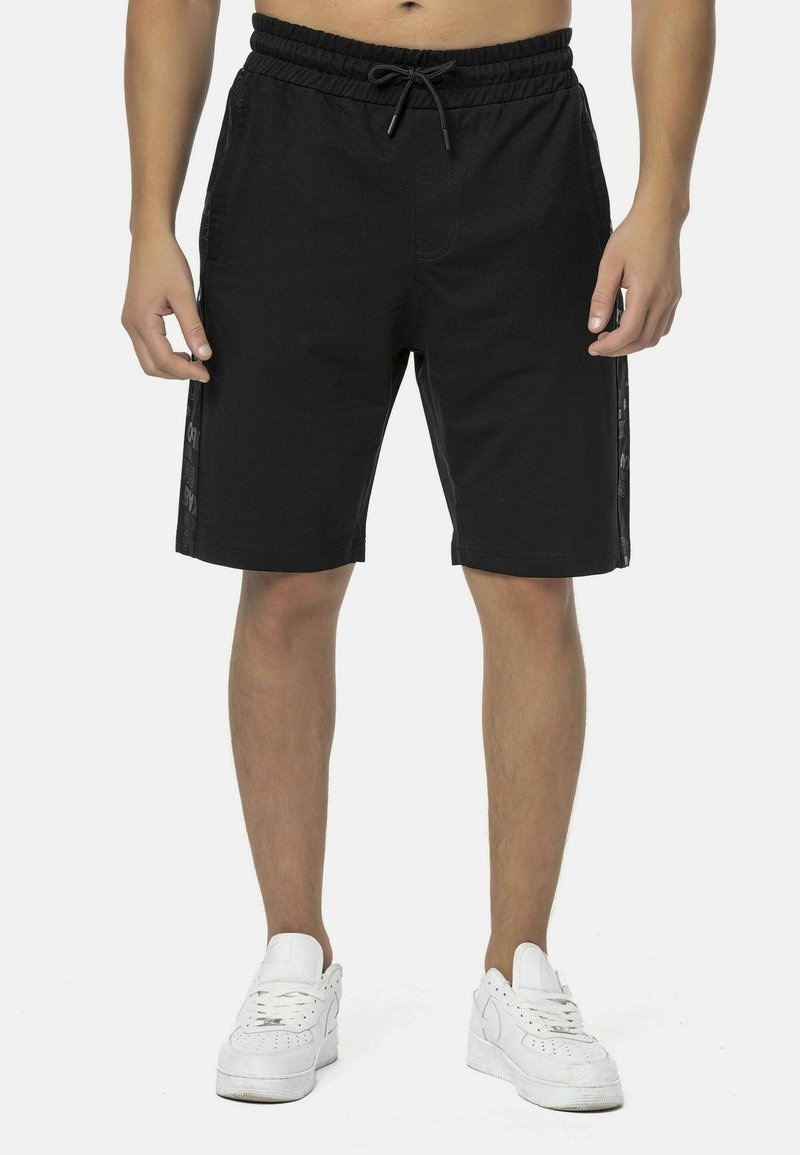 Schwarze Shorts aus Baumwolle mit einem elastischen Bund und Kordelzug. Seitliche Streifen mit strukturierten Mustern.