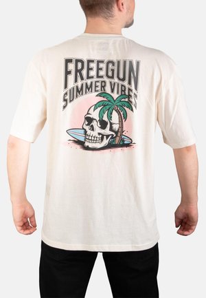 Homme portant un t-shirt blanc avec un motif dans le dos représentant un crâne, un palmier, une planche de surf, et le texte « FREEGUN SUMMER VIBES ».