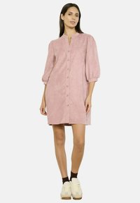 Abito rosa con bottoni e maniche a sbuffo corte, realizzato in materiale morbido. Presenta un colletto alla mandarina e una vestibilità comoda. Stile casual con delle sneakers.