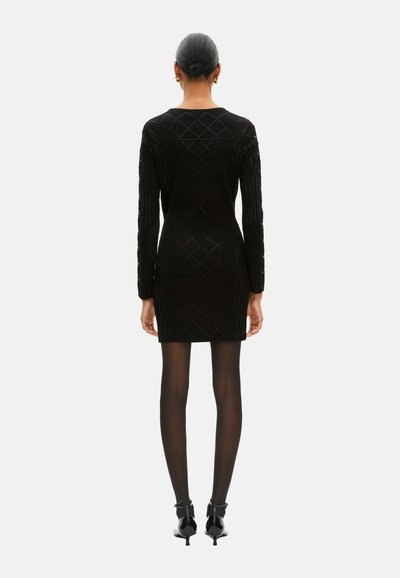 Zwarte gebreide jurk met een aansluitend silhouet, lange mouwen, ruitpatroon en een lengte tot halverwege de dij. Draagt bijpassende doorschijnende zwarte panty's en hakken.
