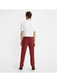 Pantaloni in corduroy rossi con una vestibilità slim, dotati di tasche posteriori e passanti per cintura, abbinati a una t-shirt bianca a maniche corte.