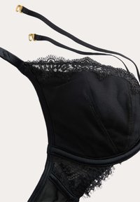 Czarny stanik z koronkowym wykończeniem, z siateczkowymi panelami, regulowanymi ramiączkami i akcentami w kolorze złotym. Teksturowany materiał z elementami bezszwowymi.