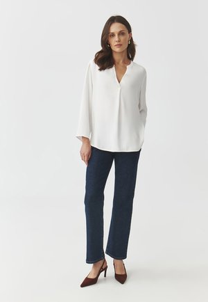White long-sleeve blouse with a V-neck, paired with dark blue denim jeans and brown pointed-toe heels. Smooth fabric, relaxed fit.