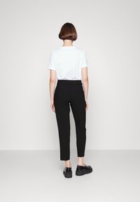 Camiseta blanca de algodón combinada con pantalones negros de corte slim. Los pantalones tienen cintura alta y bolsillos en la parte trasera. El conjunto se completa con mocasines negros gruesos.