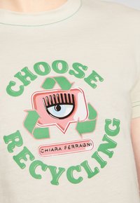 Béžové tričko se zeleným nápisem "VYBERTE RECYKLACI" obklopujícím růžovou bublinu řeči se zrakem a recyklačními šipkami; pod tím "CHIARA FERRAGNI".