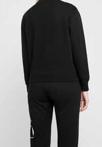Sudadera negra con mangas largas, cuello redondo y puños y dobladillo acanalados. Tiene una textura suave y un corte holgado.