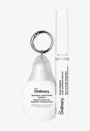 Two skincare products: a white, pear-shaped lip balm with a silver keyring and a white tube of brow serum with black text.