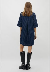 Dunkelblau gestreiftes Kleid mit kurzen Ärmeln, lockerer Passform, Rückenschlitzdetail, kombiniert mit kniehohen schwarzen Lederstiefeln.